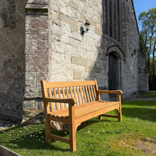 Load image into Gallery viewer, Wooden bench in front of a stone building with a clear blue sky.
