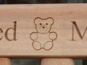 A Teddy bear symbol carved into wood on a memorial bench - 4mb2756